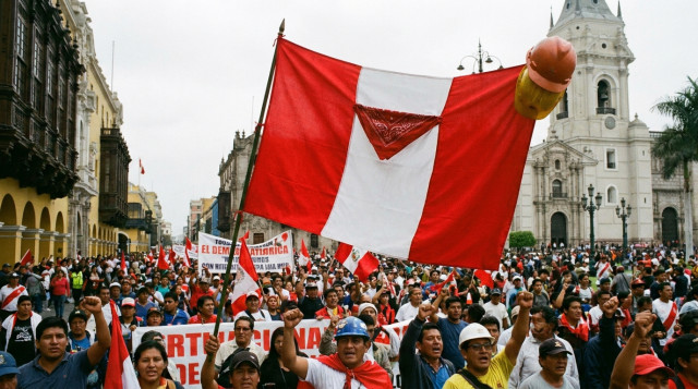 bandera roja y blanca con pañuelo y casco de trabajador durante una manifestación del 1 de mayo en una calle de Lima